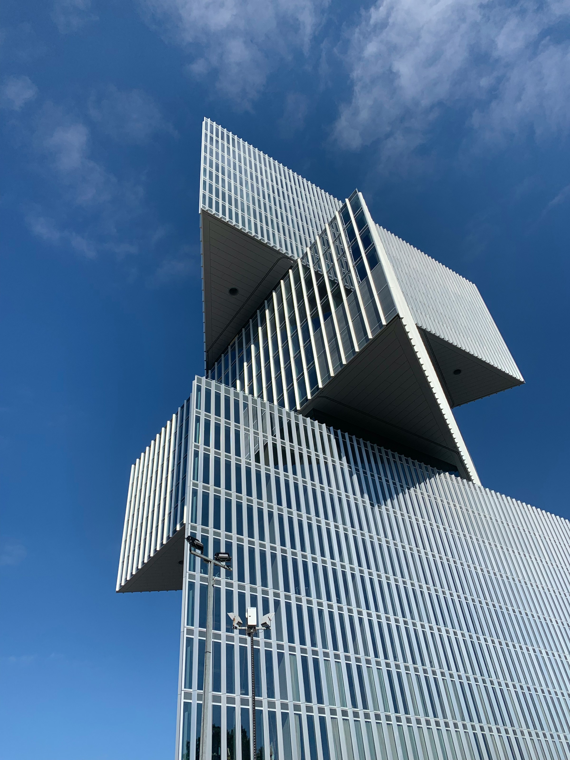 Edifício de geometria angular em vidro e aço recortado contra o céu claro.